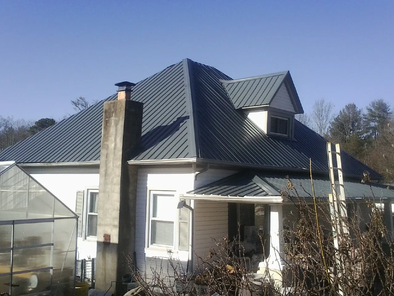 Dark blue standing seam metal roof on a white farmhouse with dormer — Slate & Tile Roof Repair by Roofing Brothers in Miamiville