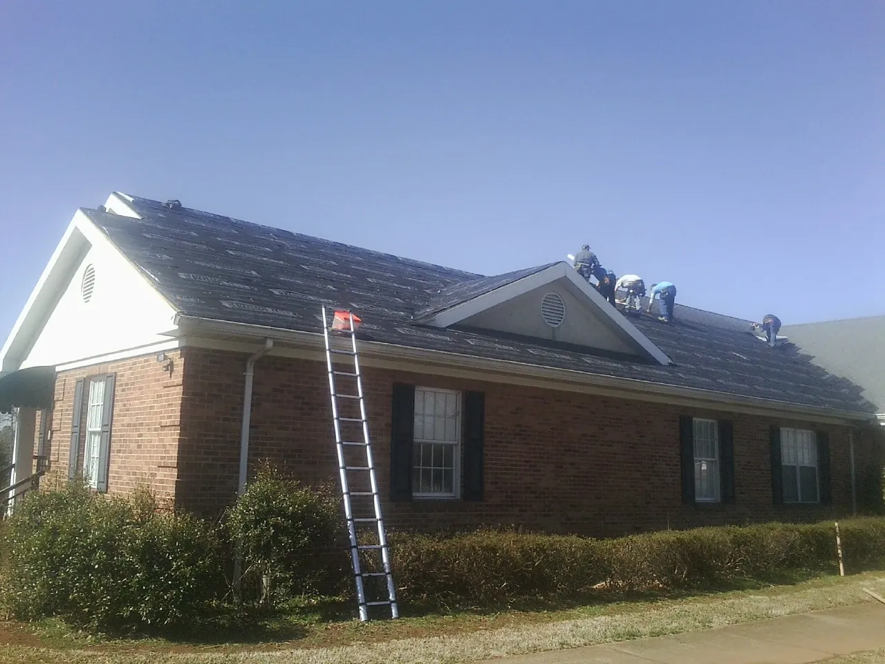 Crew tearing shingles off a brick ranch roof with a ladder set — Emergency Roof Repair work by our crew in Miamiville