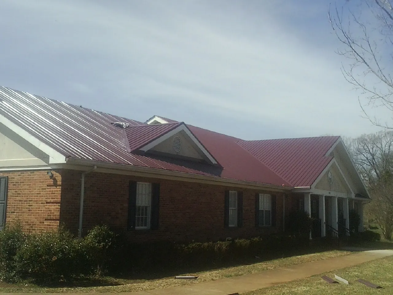 Red metal roof with gabled entries on a long brick building, from a Hail Damage Roof Repair job in Miamiville