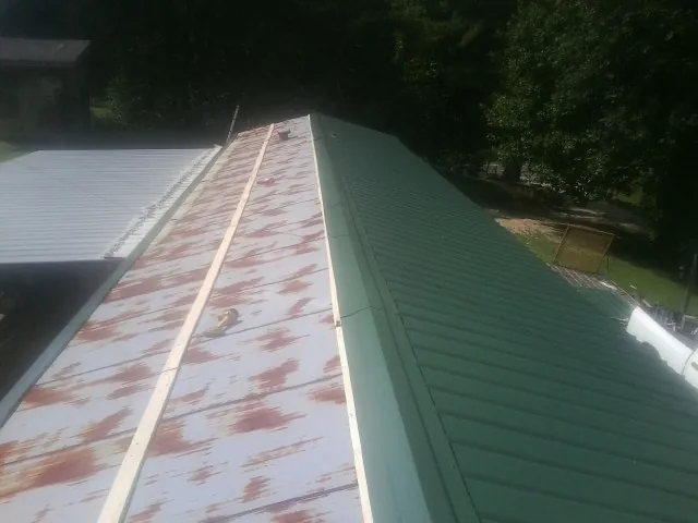 Old rusted panels beside newly installed green metal roofing — Wind Damage Roof Repair by Roofing Brothers in Miamiville