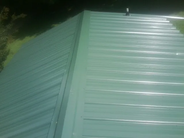 New green metal panels meeting at the ridge of a roof — Flat Roof Repair work by our crew in Miamiville