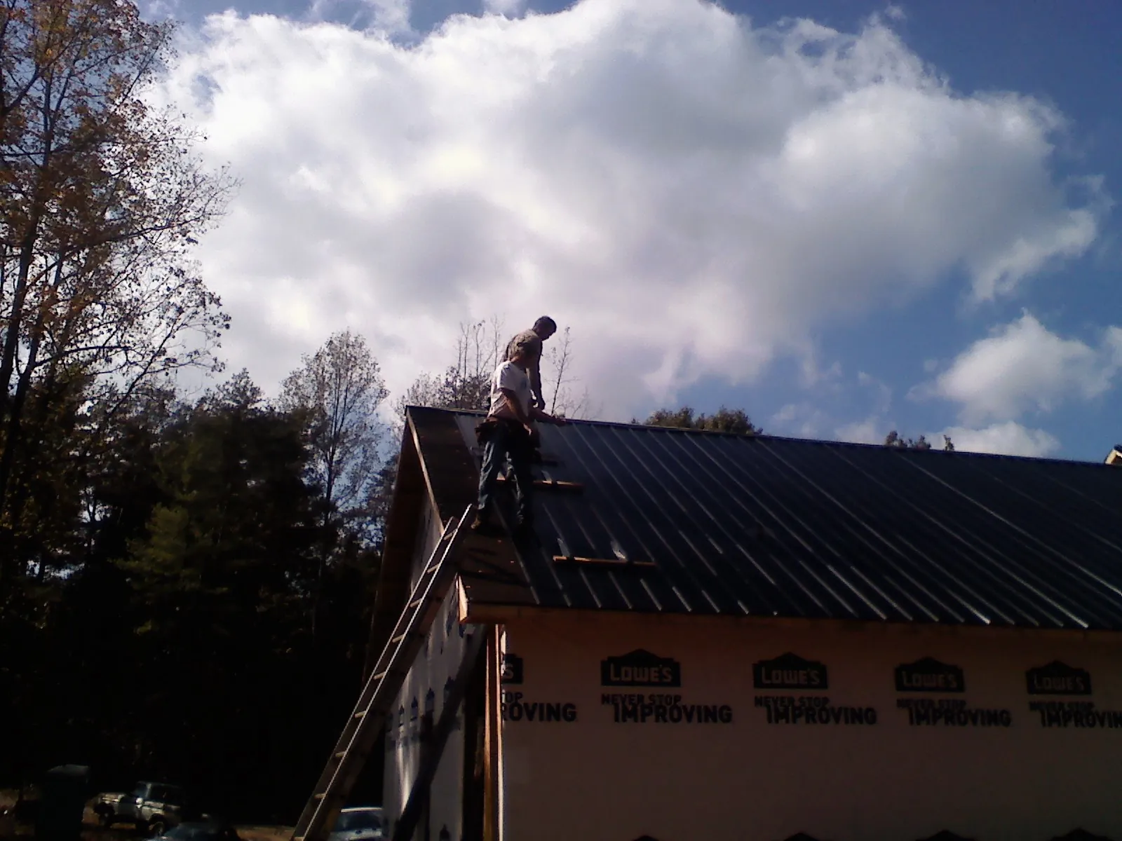 Roofer fastening dark metal panels high against a cloudy sky, from a Roof Inspection job in Miamiville