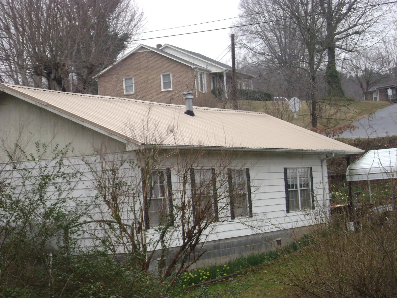 Tan metal roof on a white sided house set into a hillside — Commercial Roofing by Roofing Brothers in Miamiville
